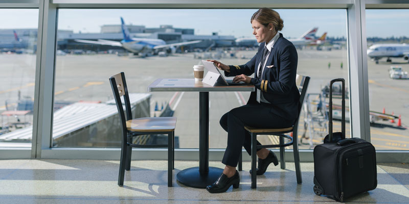 Female pilot sits in an airport café using a Surface device