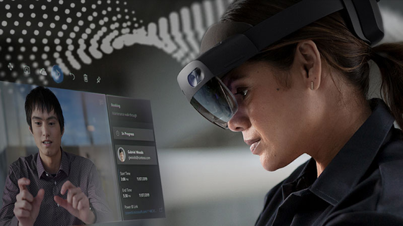 A woman wearing a HoloLens 2 headset receives instruction via her desktop PC
