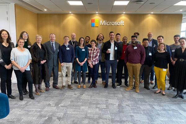 A Group of people standing smiling with the Microsoft logo behind them