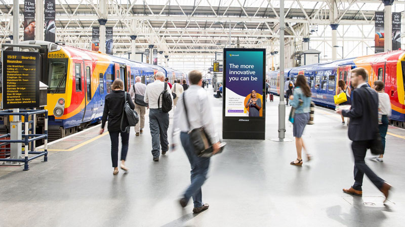 People walking in a train station with Microsoft's BSL digital billboards